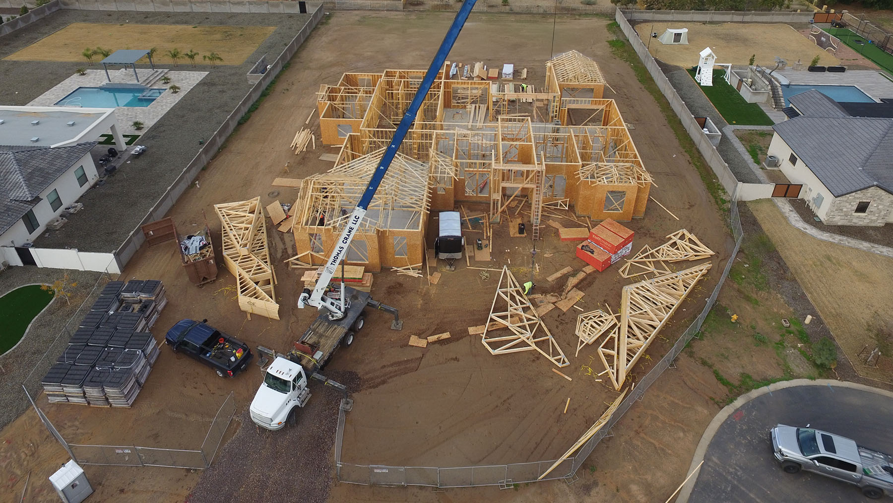 Aerial view of a custom home construction site in Utah, showcasing wooden framing, a crane in action, and surrounding residential properties — highlighting expert residential building and luxury home development.