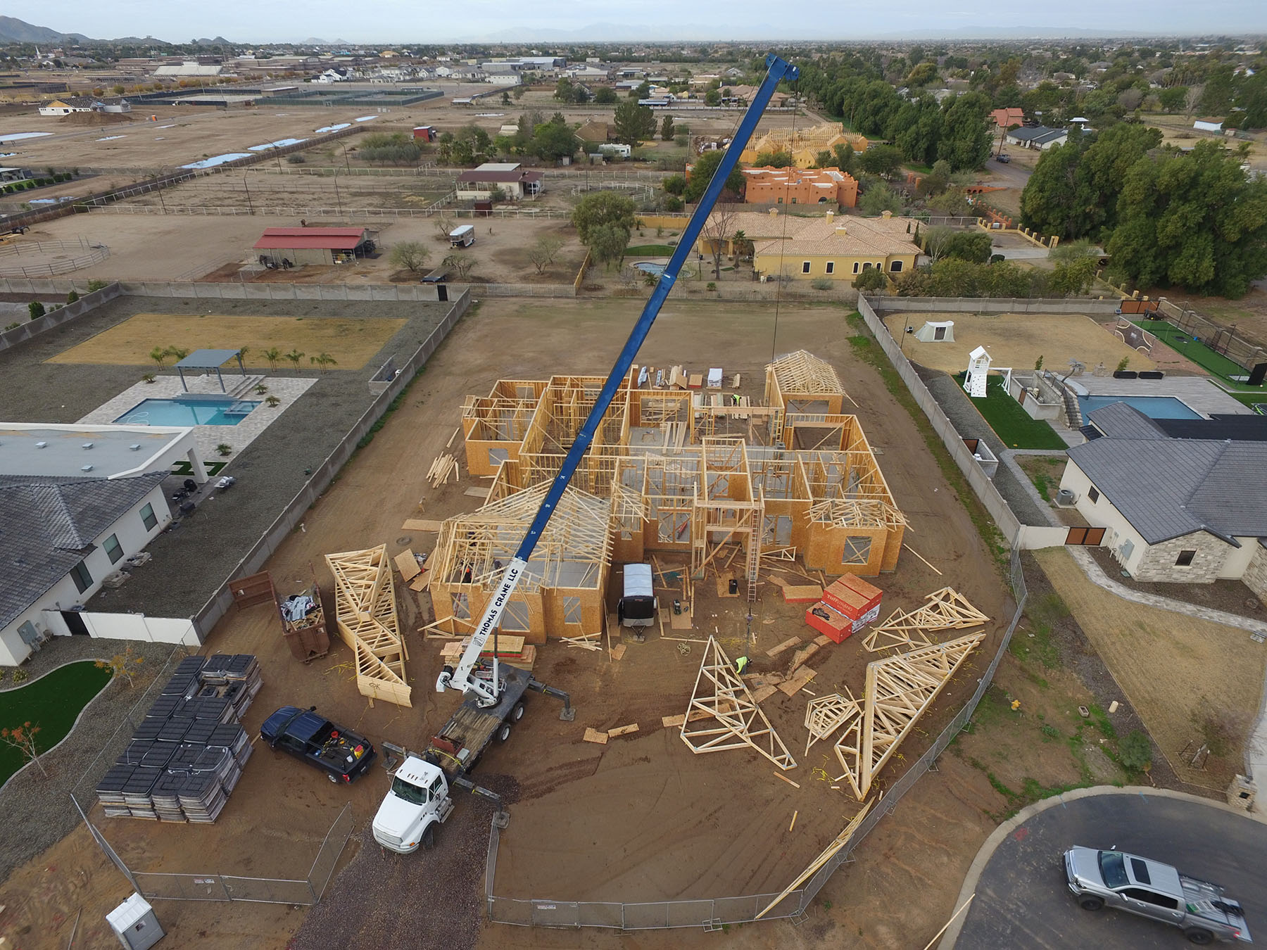 Aerial view of a custom home construction site in Utah, showcasing wooden framing, a crane in action, and surrounding residential properties — highlighting expert residential building and luxury home development.